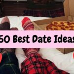 Cozy stay-at-home date night idea. Two people wearing festive red and green patterned socks are lying on a white bed with a large pepperoni pizza in a box beside their feet, ready to eat. A pink banner overlay reads '50 Best Date Ideas'. Red and pink heart emojis decorate the image. This photo illustrates a relaxing, budget-friendly indoor date for couples looking for fun, romantic relationship ideas in 2025.