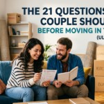 A young, smiling couple sits on a sofa in a bright living room surrounded by cardboard moving boxes. They are looking at a checklist titled "21 Questions" while holding a notebook, appearing to have a positive conversation. The text overlay reads: "The 21 Questions Every Couple Should Ask Before Moving In Together (Ultimate Guide).