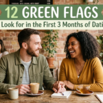 A happy, diverse couple sits at a rustic wooden table in a cozy, sunlit cafe filled with green plants. They are holding hands and smiling warmly at each other over coffee and tea. A green and cream banner overlay at the top reads '12 Green Flags To Look for in the First 3 Months of Dating' with small leaf illustrations