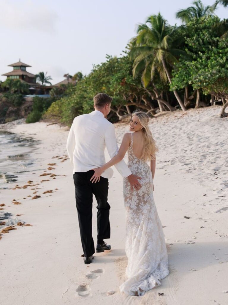 Jimmy Donaldson (MrBeast) and his bride walking hand-in-hand along a tropical sandy beach in their wedding attire.